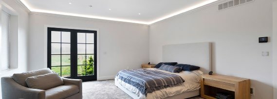 Loxone Elevated plan — bedroom with warm ambient cove lighting and a Loxone Touch panel
