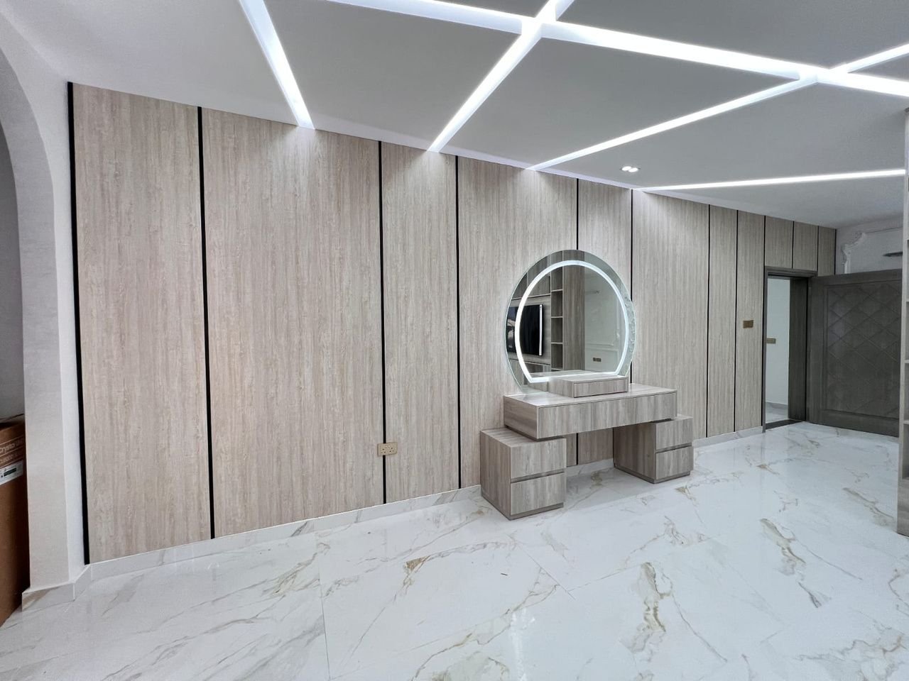 Backlit round mirror above a built-in dressing table against wood paneling