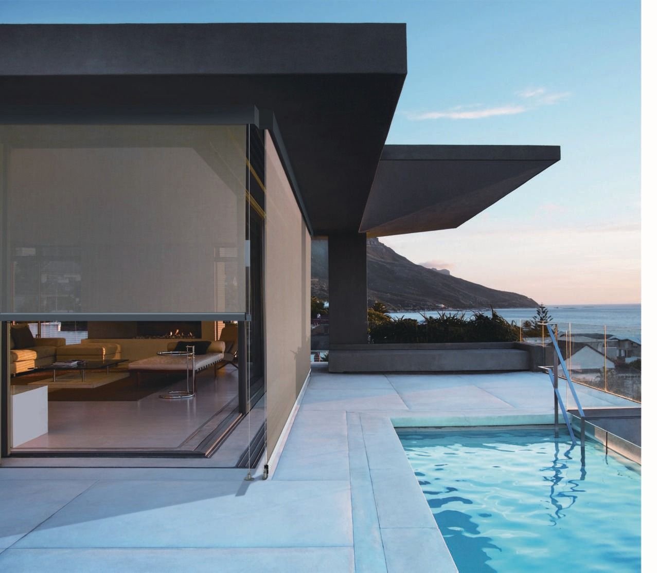 Retractable external screen shading a glazed terrace beside a pool with a sea view